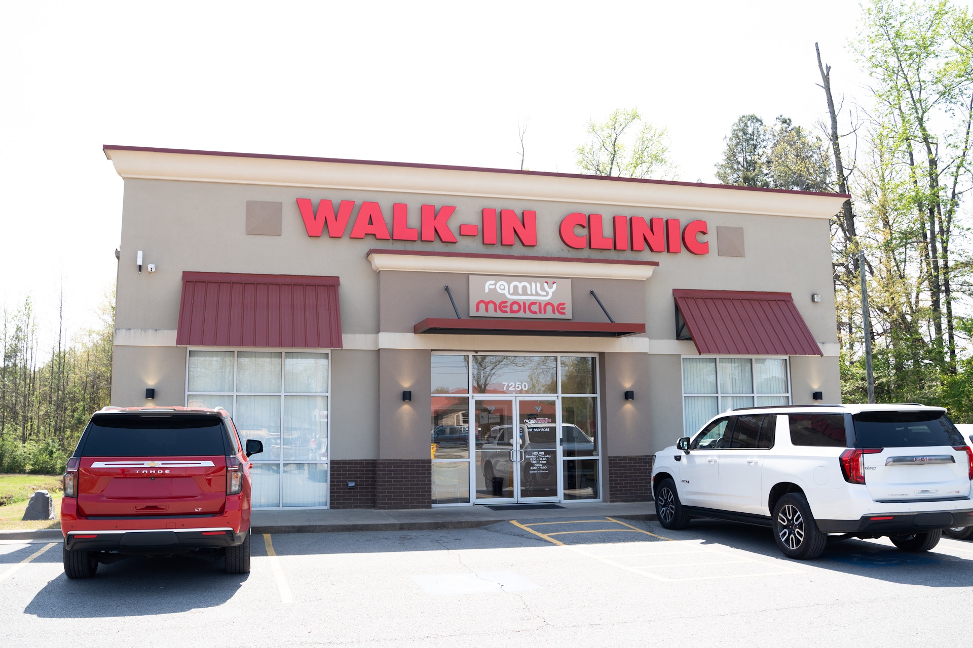 A medical building with a large WALK-IN CLINIC sign above the entrance, Family Medicine below it, and two SUVs parked in front of the clinic on a sunny day.