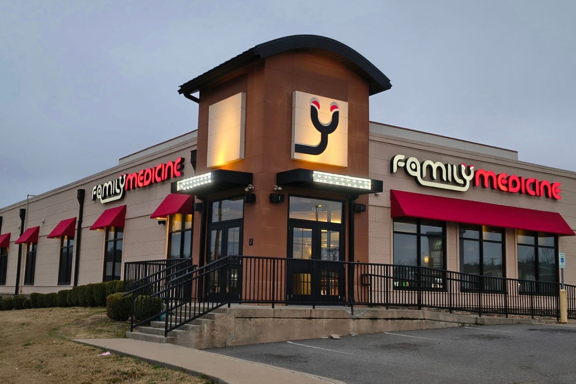 A one-story building with red awnings and a sign reading Family Medicine in large letters above the entrance. There is a ramp leading to the front doors and bushes along the side.